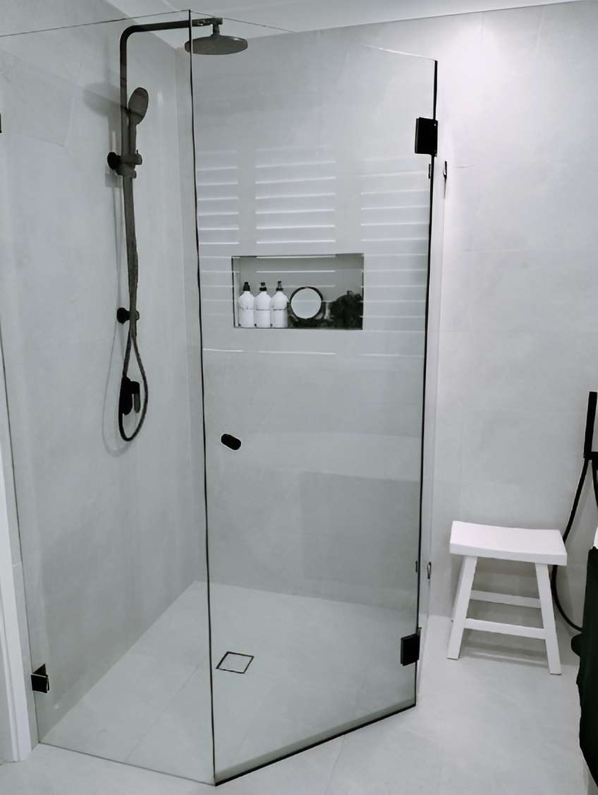 Frameless corner shower with a black rail shower, tiled niche and a small white stool