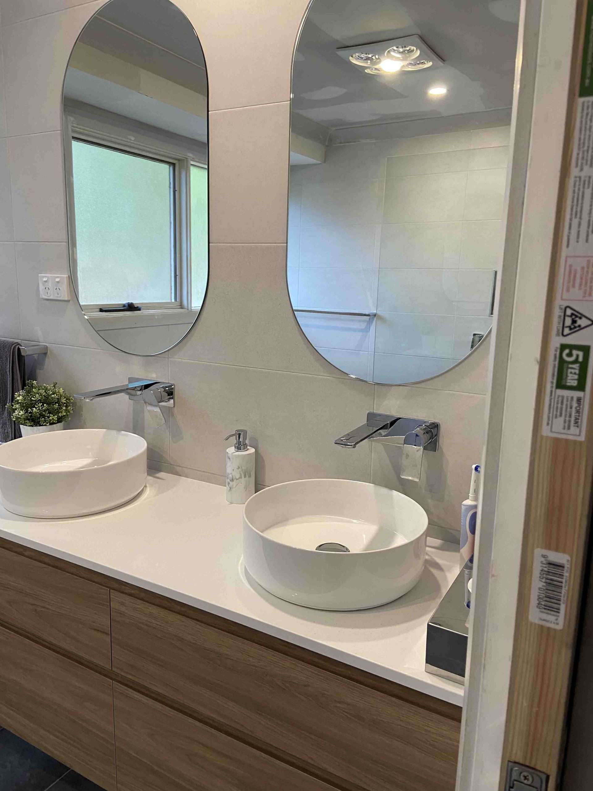 Two vessel basins on a timber-look vanity below two oval mirrors