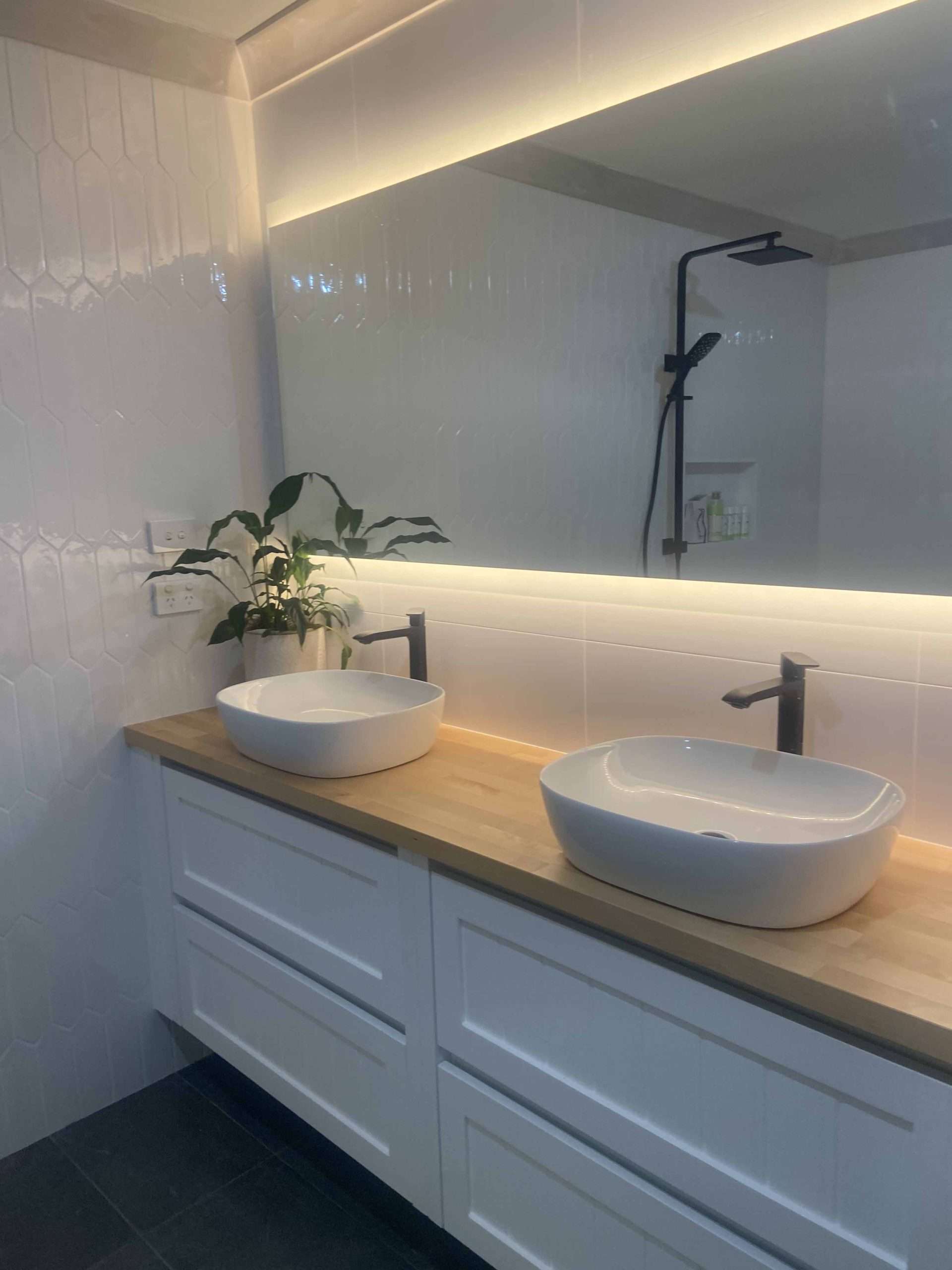 White shaker-style vanity with a timber top, two vessel basins and an LED-lit mirror