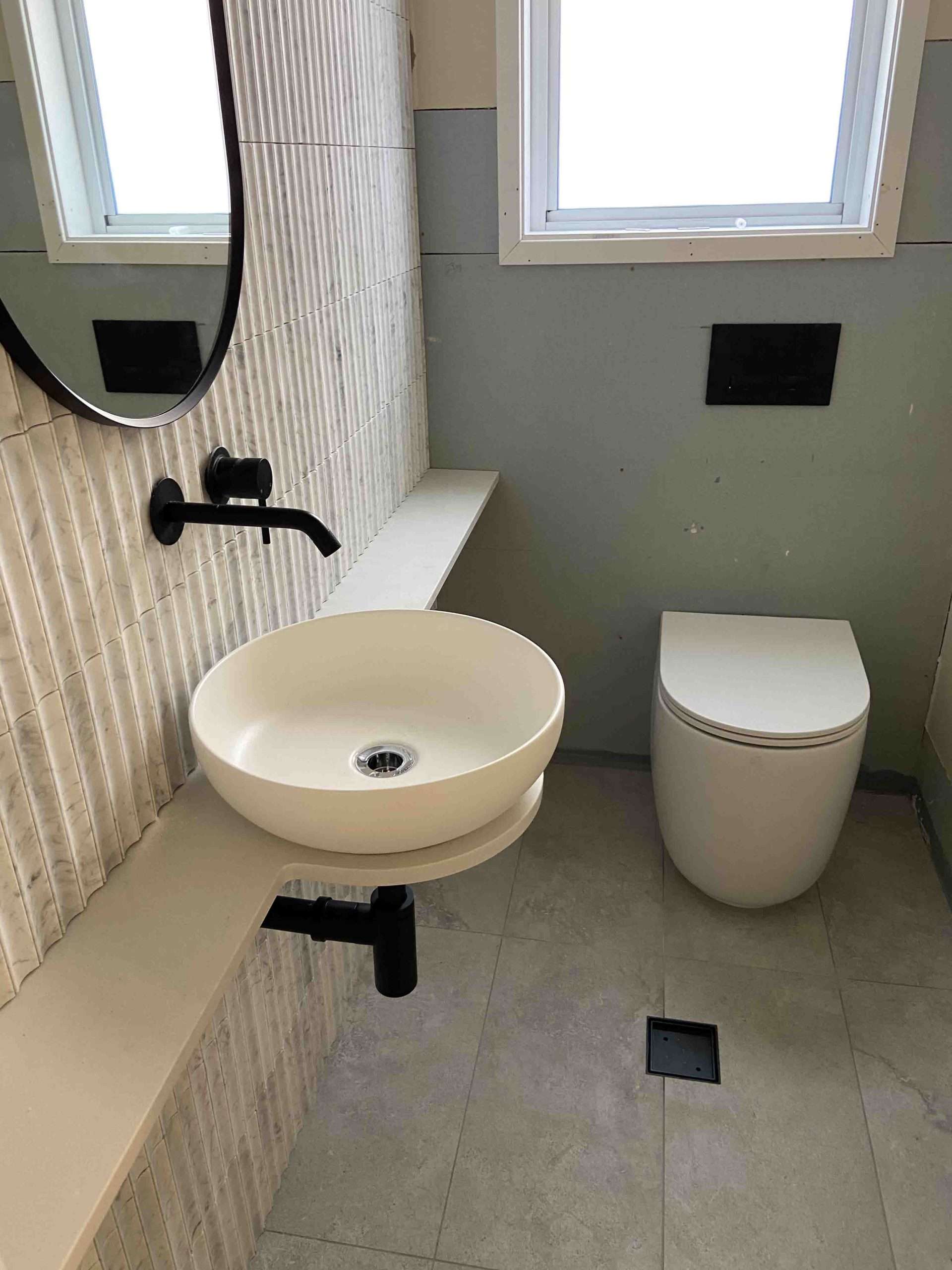 Bathroom with a round basin on a floating stone shelf, black tapware and a white toilet