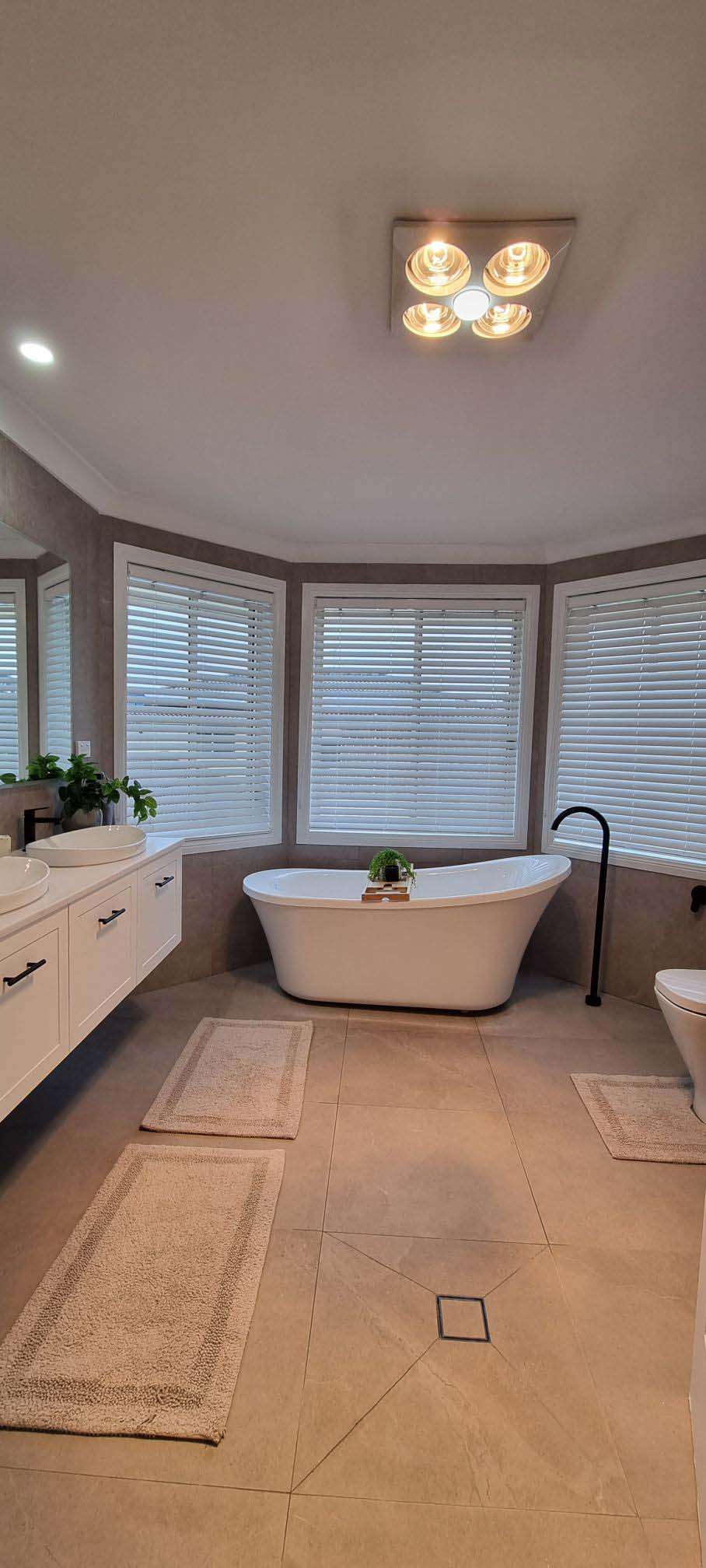 Large bathroom with a freestanding bath in a bay window, white vanity and heat lamp