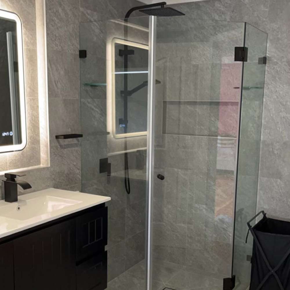 Glass shower enclosure with black fittings next to a dark vanity and LED mirror
