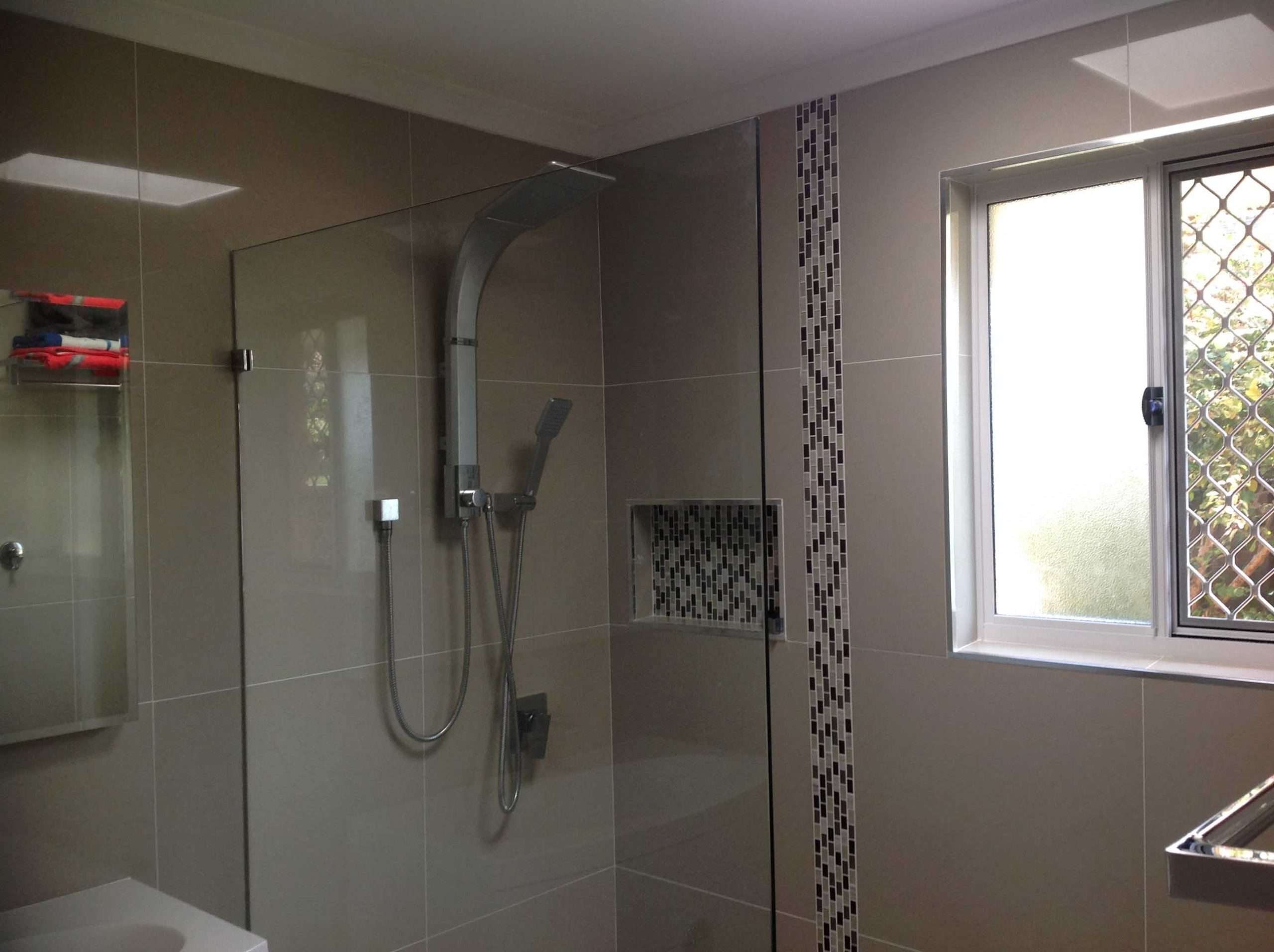 Shower with a glass panel, shower column, mosaic tile strip and niche beside a window