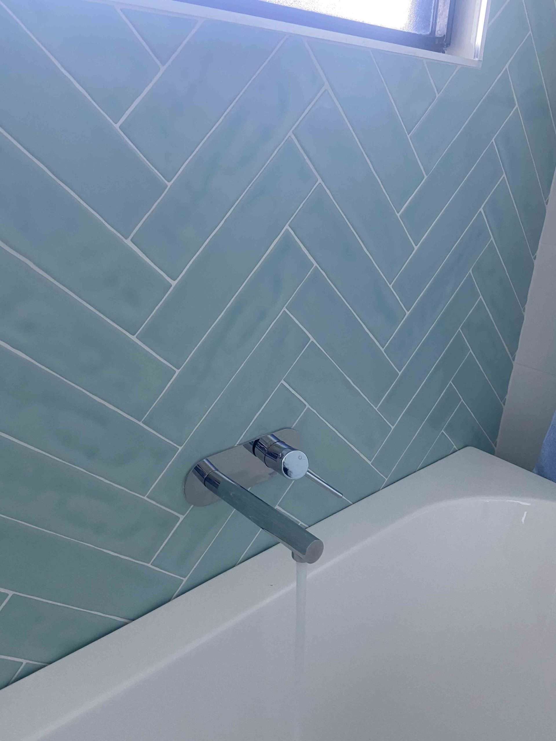 Bath with a chrome wall spout and green herringbone wall tiles